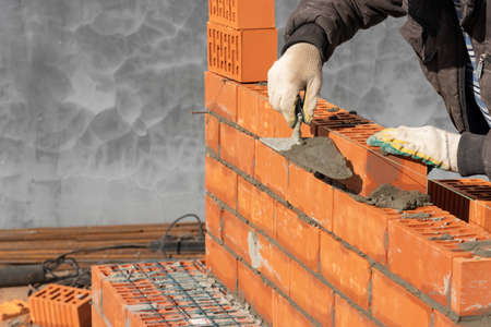 Laying of red bricks by a builder, building a task wall.