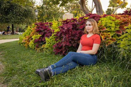 Woman with blue jeans and red t-shirt resting and posing in front of a red plantsの写真素材