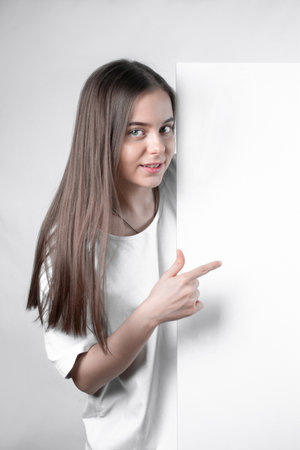 Girl teenager demonstrating a blank sheet of paper shows a finger.の写真素材