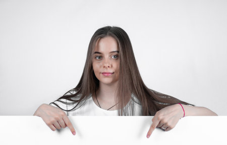Nice teen girl shows down with two fingers on a white poster.の写真素材