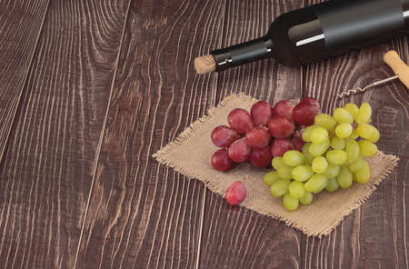 Wine bottle with blank matte black label and grapes lies on a background of wooden boardsの写真素材