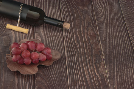 Vintage red wine bottle with blank matte black label, corkscrew on a grunged wooden table backgroundの写真素材