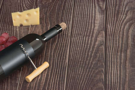 Wine bottle with blank matte black label, grapes and cheese lie in the backgroundの写真素材