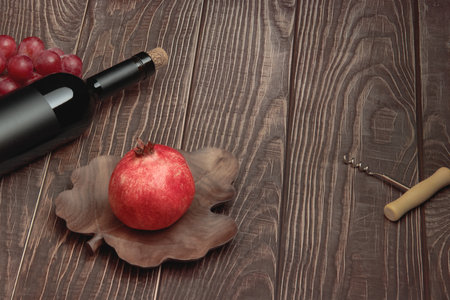 Expensive wine bottle with corkscrew, pomegranate and grapes on textured wooden tableの写真素材