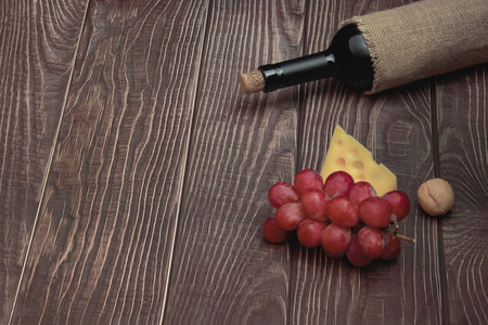 Wine bottle, grapes and cheese lie on the background of wooden boardsの写真素材