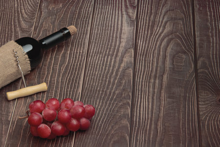 Expensive wine bottle with corkscrew and grapes on conceptual wooden boardsの写真素材