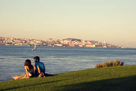 Young couple sitting on banks of river Tejo in Lisboa with view to the city, Portugal