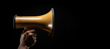 Generative AI, golden megaphone in hand on an empty black background, panoramic image with copy spaceの素材