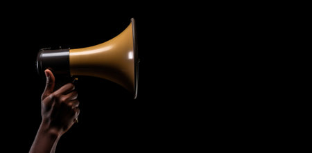 Generative AI, golden megaphone in hand on an empty black background, panoramic image with copy spaceの素材