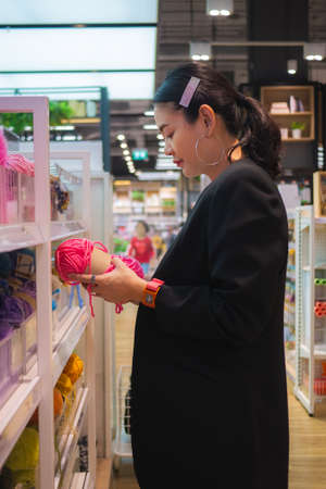 Asian working woman choosing a pink yarn in department store. Knitting accessories