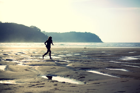 Backlight of a litlle girl running on the beach. Cross processing effect.の写真素材