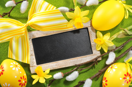 Easter blackboard with copy space, yellow easter eggs, narcissus and pussy willow on tableclothの写真素材
