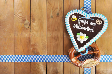 Regards from the Oktoberfest - original Bavarian salted pretzel soft and Oktoberfest gingerbread heart from Germany in front of wooden boardの写真素材