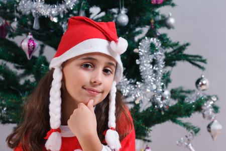 Portrait of happy girl dressed as Santa Claus next to Christmas tree.の写真素材