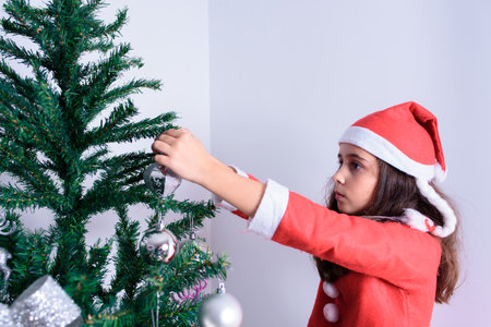Little girl decorating Christmas tree. Disguised as Santa Claus. On white backgroundの写真素材
