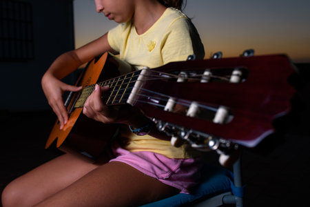 Brunette girl playing acoustic guitar outdoors during sunset. Close-up of the guitar headstock. Focus on fingers pressing the strings of the neck.の写真素材