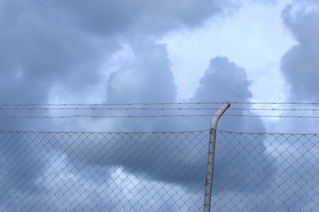 Metallic net against dark stormy clouds sky. Concepts of despair and fearの写真素材