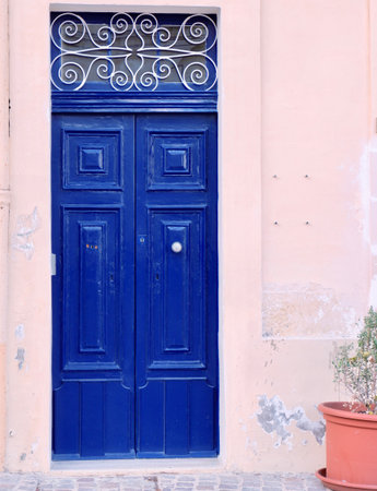 Old fashioned deep blue double door from outside. Closed aged entrance to offices or apartment in classical style with metal ornamental forged element on top. Vertical photo.の写真素材