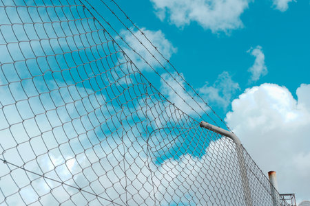 Industrial metallic net against cyan blue sky with cumulus clouds.の写真素材