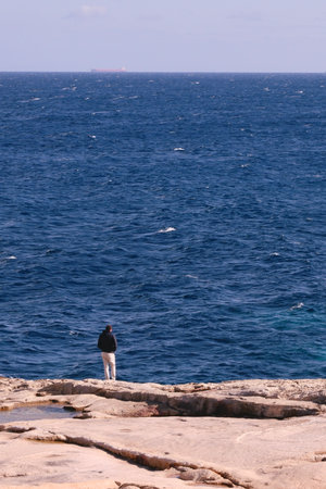 Vertical picture of lined seaside landscape in winter. Man in solitude looking at sea in winter. Rocky seaside of Marsascala, Malta. Conceptual ideas of solitude and lonelinessの写真素材