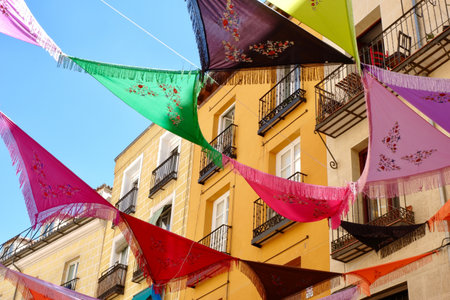 Multicolored Spanish shawls are strung between the balconies outside on the street. The decorated ambient creates a festive mood. La Latina district, Madrid, Spainの写真素材