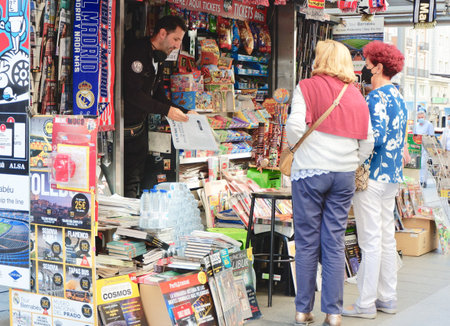 Madrid, Spain - October 12, 2021: elder Spanish women in virus protective masks buying newspapers from local vendor in kiosk on touristic street of Gran Viaのeditorial素材