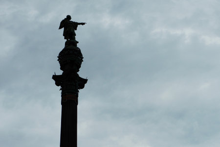 Silhouette of the statue of Christopher Columbus with hand pointing direction to America from Barcelona, Spain. Moody gray sky on the backgroundの写真素材