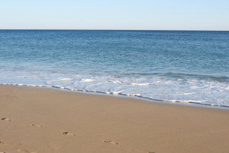 Calm ocean side with wet sand under clear blue sky in Algarve, Portugal.の写真素材