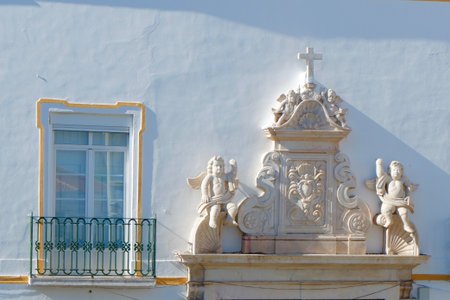 Old wall with stucco decor with a cross, angels and window of the vintage building in Elvas, Portugal.の写真素材