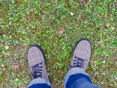 Looking down on female legs wearing fancy gray boots and jeans standing on green grass field....