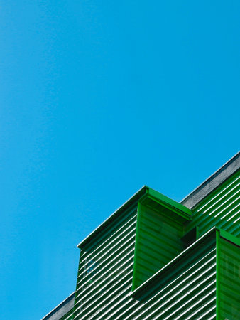 Edge of a city building with a modern lined facade of green color against blue clear sky. Copy...