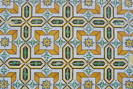Aged ceramic tiles of faded yellow color with geometric ornament on the weathered shabby facade in...