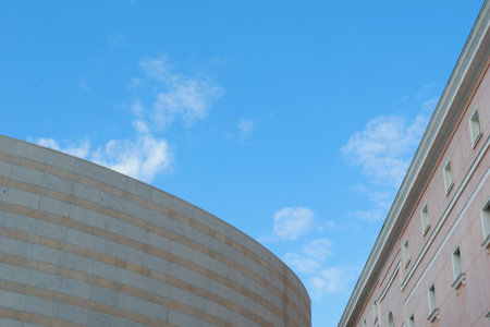Two distinct buildings showcase a blend of modern and traditional architecture, positioned against a bright blue sky filled with light clouds. This urban landscape highlights cultural heritage.の写真素材
