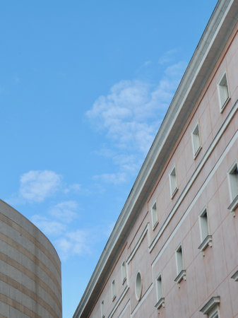 Bright blue sky with a few clouds complements unique architectural lines of buildings. The structures feature a mixture of textures and colors, showcasing contemporary design elements.の写真素材
