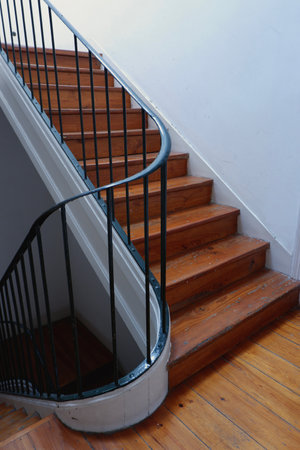 A curved staircase with polished wooden steps leads upward, showcasing a simple yet elegant design that enhances the interior space. Natural light defines the atmosphere.の写真素材