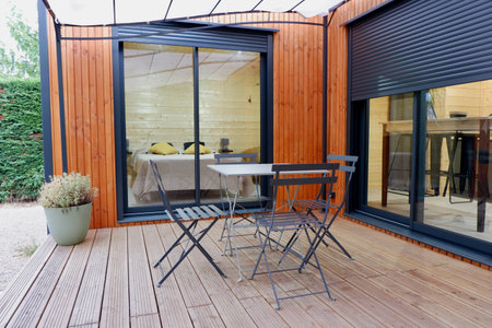 A cozy outdoor seating area showcases a sleek table and chairs against wooden walls, framed by large windows that offer views of nature, perfect for relaxation.の写真素材