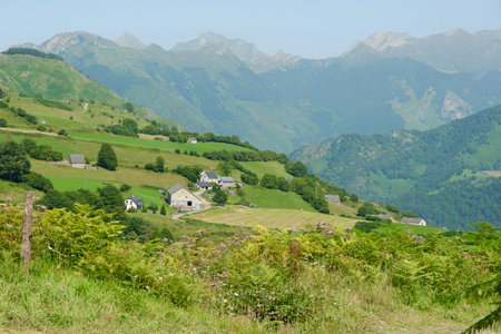 Lush green hills cradle small houses, showcasing a peaceful rural landscape in the mountains on a clear sunny day, perfect for outdoor exploration and tranquility.の写真素材
