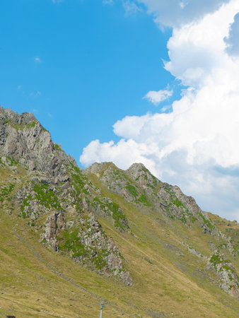 Rocky mountain terrain features lush greenery and a clear blue sky with scattered clouds. A serene...