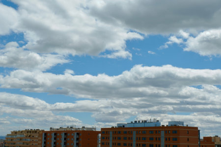 Fluffy white clouds drift across a bright blue sky above modern residential buildings. It is a sunny day with a nice view of the cityscape below.の写真素材