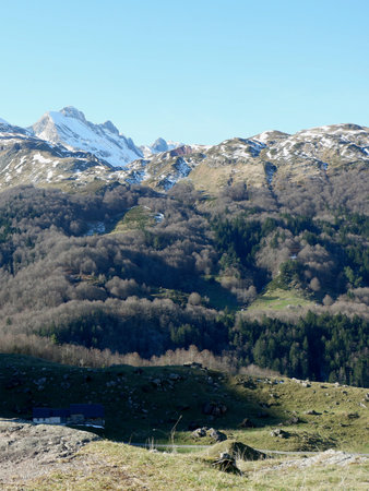 Snowy peaks tower over lush green valleys beneath a bright blue sky. The landscape showcases the beauty of nature in a tranquil setting during springtime.の写真素材