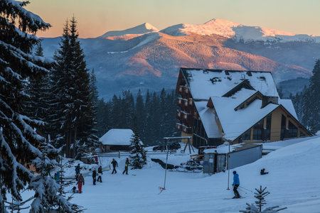in the snow-capped mountains of the Carpathians people ski on the ski track. on the mountain there is a wooden house. around the green snowy firの写真素材