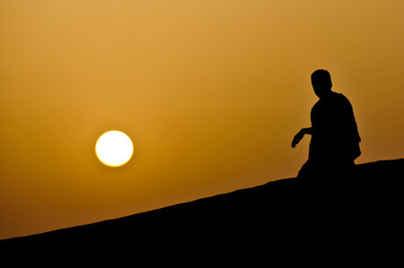 Kneeling man, overlooking sunset in the deserts of Dubai, UAE の写真素材