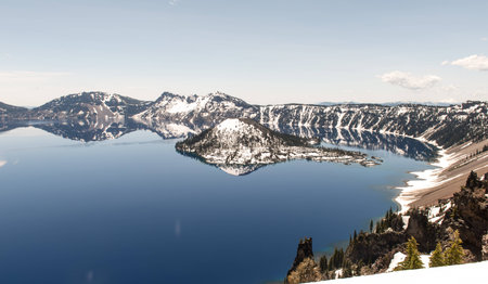 Clear blue water of Crater Lake National Park in Oregon during early spring with some snow left from winter. Wizard Island in the distance.の写真素材