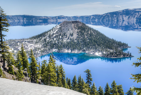 Wizard Island and the clear blue water of Crater Lake National Park in Oregon during late spring with some snow left from winter.の写真素材