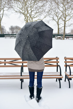 Girl out in a snowstorm in the park, with an umbrella to shield her.の写真素材