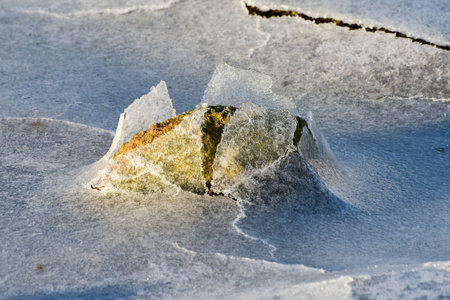 Rock cracking through the ice in Boosen in the Lofoten Islands, Norway in the winter.