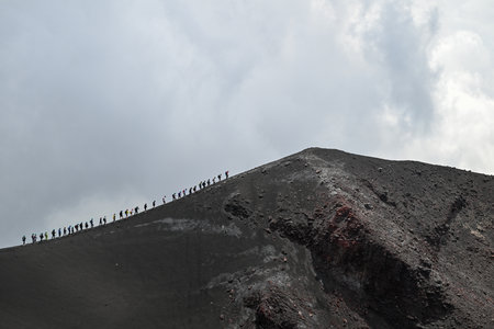 Hikers along Mount Etna, Sicily - Tallest active volcano of Europe 3329 m in Italy. Panoramic wide view of the active volcano Etna, extinct craters on the slope, traces of volcanic activity.の写真素材