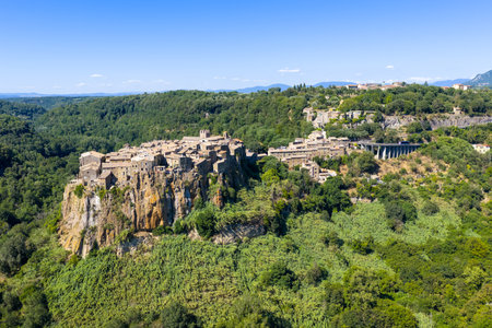 Aerial view of the medieval village of Calcata, Italy, perched on a cliff surrounded by dense forest...