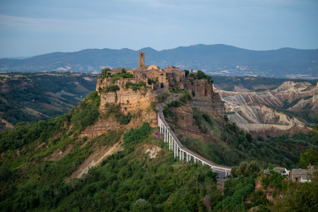 Civita di Bagnoregio, a picturesque hilltop village in Italy, bathed in soft morning light with surrounding lush greenery and clear skies.の写真素材