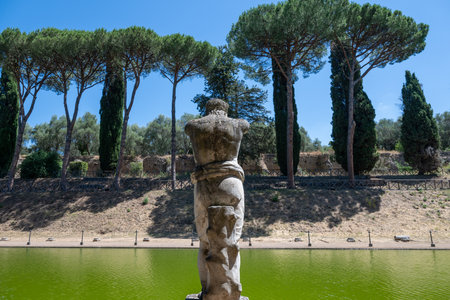 Villa Adriana, Tivoli: Ancient Roman statue in Canopus area, Villa Adriana, Tivoli. Limestone figure by green pool, surrounded by pine trees, showcasing classical Roman landscape design.の写真素材